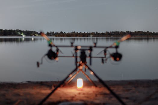 A serene fishing scene by the lake under the evening sky with equipment lit by candlelight.