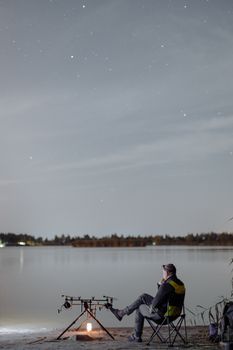 夜晚，一名男子在湖边平静地钓鱼，仰望着星空