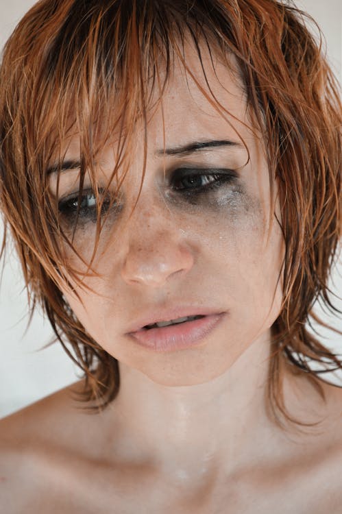 Crop desperate female with short hair bare shoulders and flowing mascara crying unhappily in studio