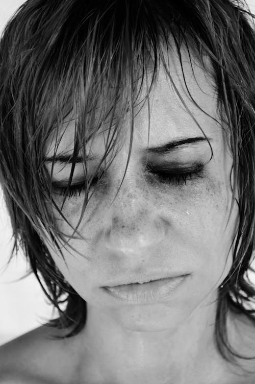 Black and white crop female with short hairstyle and bare shoulders frowning with eyes closed and crying in frustration