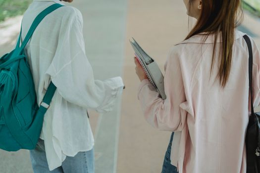 两名年轻女性背着背包和笔记本，在校园里边散步边交谈