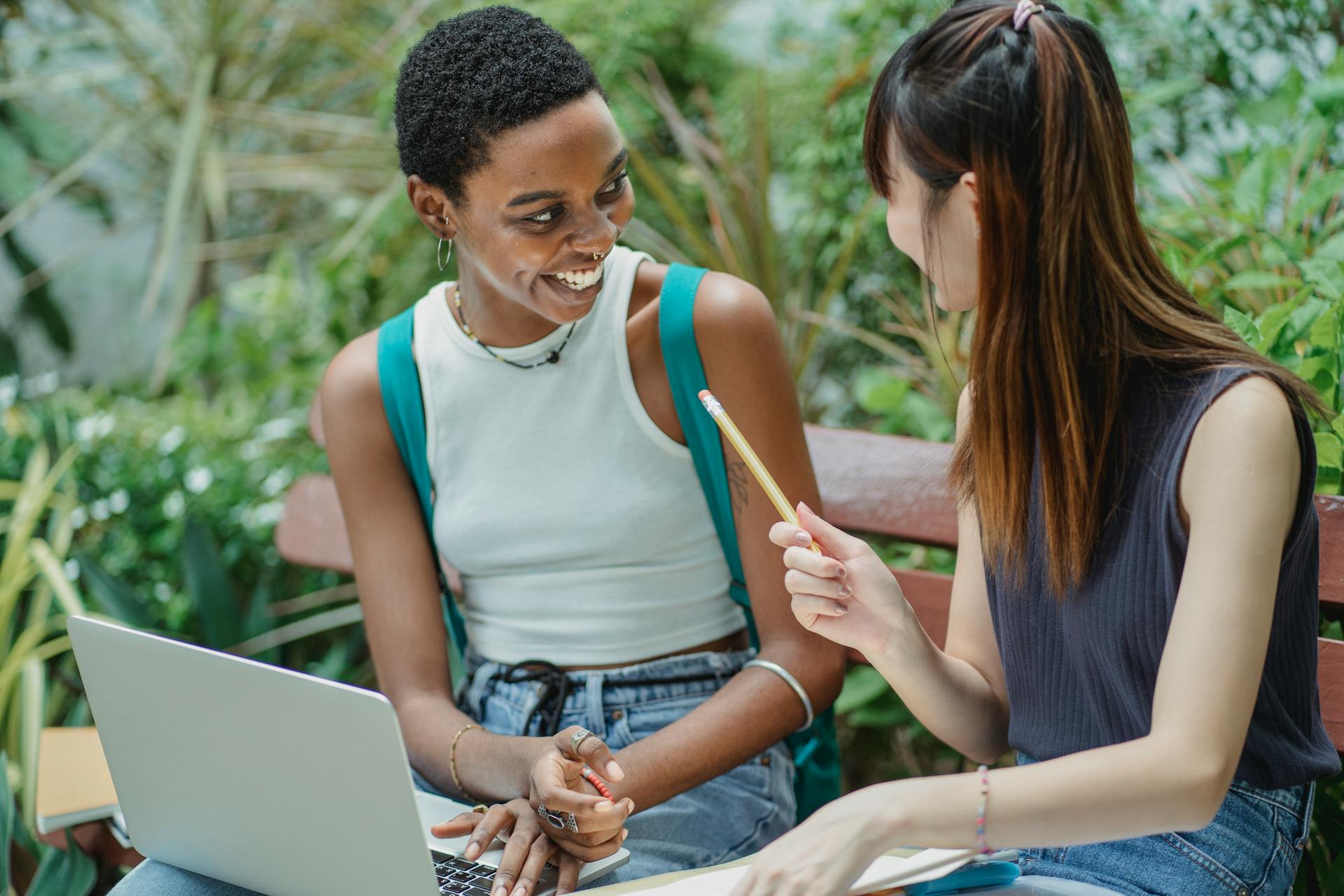 Joyful multiethnic female students working on assignment in park