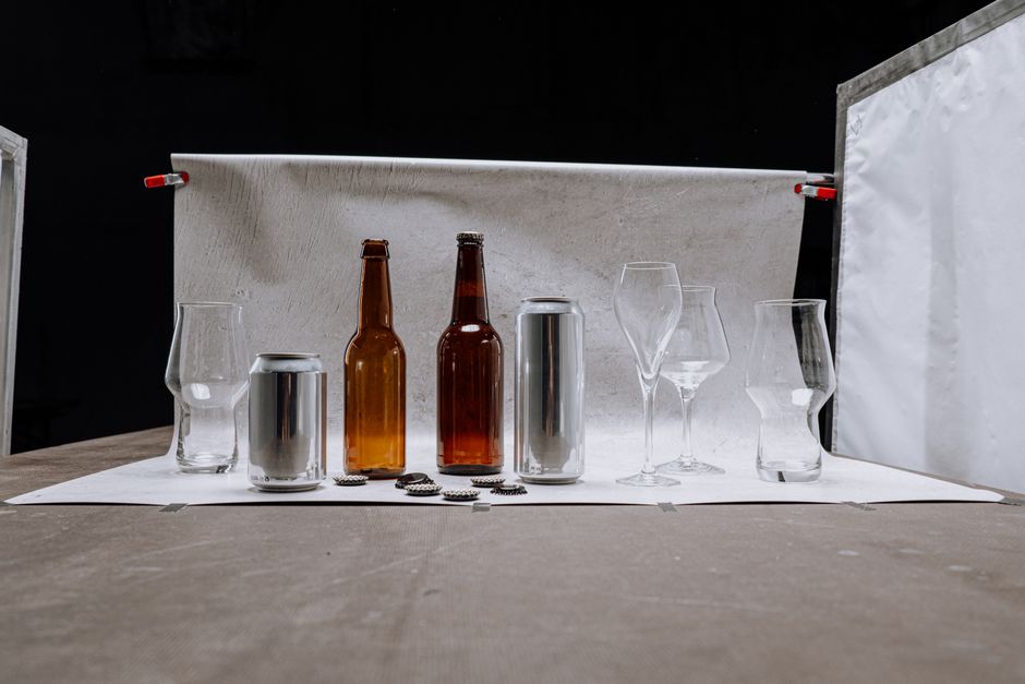A clean studio shot of beer bottles, cans, and glassware set against a neutral backdrop.