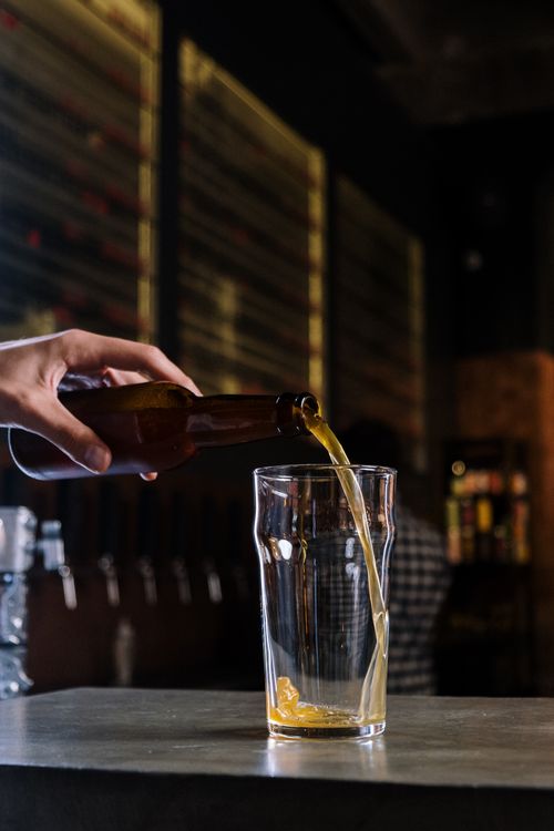 Free Hand pouring craft beer from a bottle into a glass in a dimly lit pub. Stock Photo