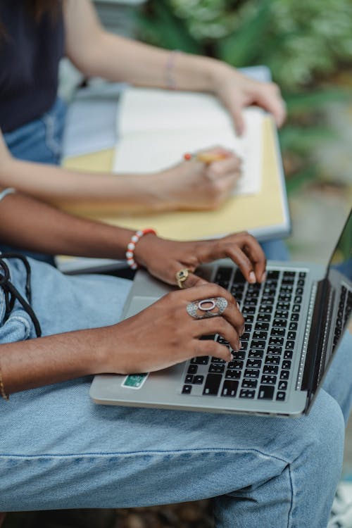 Female friends using computer writing notes in notebook