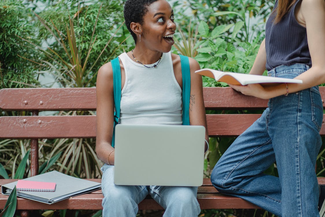 Multiethnic women talking while using computer and notebook in nature ...