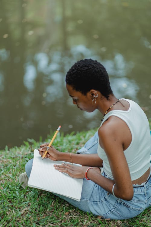 African American woman writing in diary on meadow