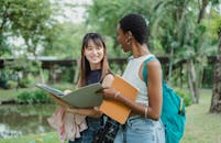 Multiethnic female friends speaking while walking in park with notepads