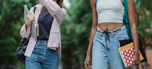 Unrecognizable crop young multiracial women standing in summer day on street with notebooks and laptop and wearing casual outfit