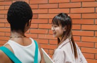 Positive multiethnic schoolgirls walking outside brick building together