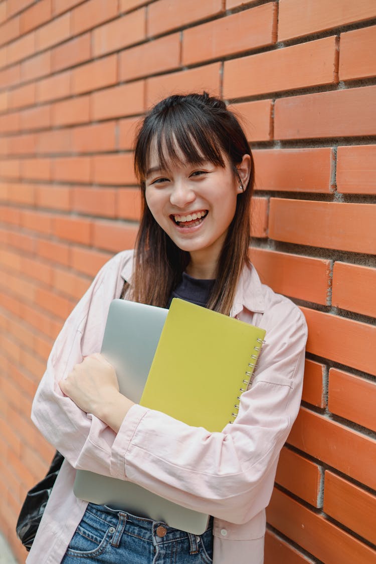 Joyful Asian Female Student Leaning On University Brick Wall