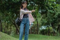 一位穿着休闲服装的快乐年轻亚洲女性在绿色公园里边散步边用耳机打视频电话