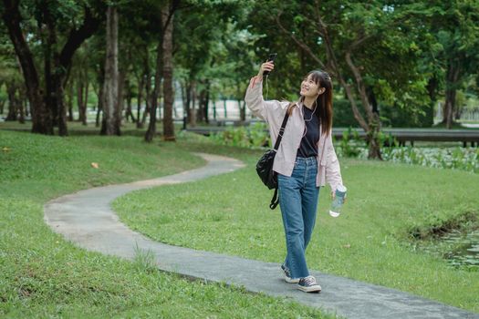 阳光明媚，一位快乐的年轻女子在绿意盎然的公园里边散步边自拍