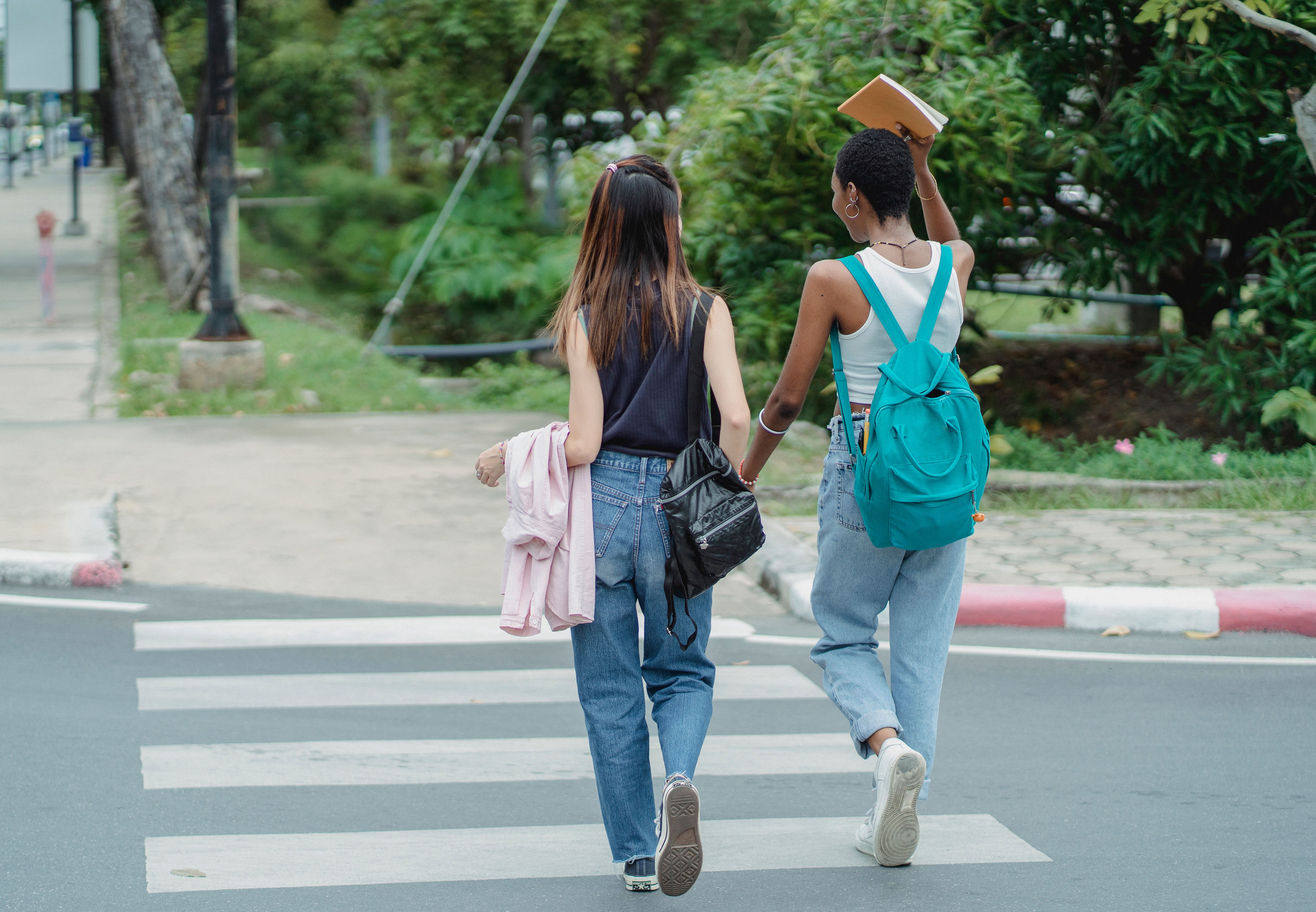 两名身着休闲装的年轻女子手牵着手，背着背包，穿过街道，在户外享受悠闲的一天