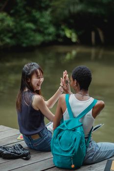几位穿着休闲装的年轻女性朋友，坐在河边的木桥上，大笑着互相击掌的背影