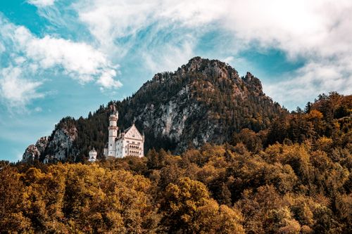 Free Iconic Neuschwanstein Castle in Bavaria amidst colorful autumn trees and mountain vista. Stock Photo