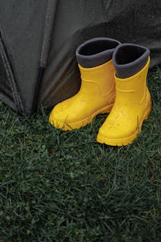 Vibrant yellow rain boots beside a wet tent on green grass, perfect weather gear imagery.