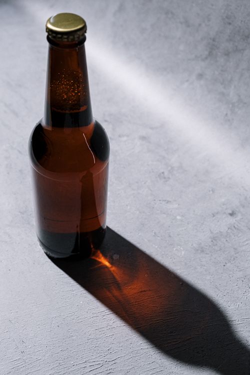 Free Craft beer bottle with dramatic shadow casting on a textured surface, studio lighting. Stock Photo