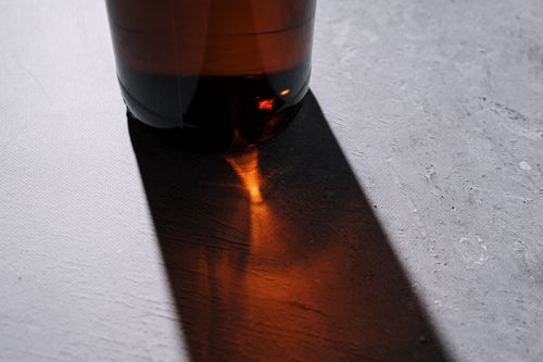 Free Close-up of a beer bottle casting a dramatic shadow on a textured surface. Stock Photo