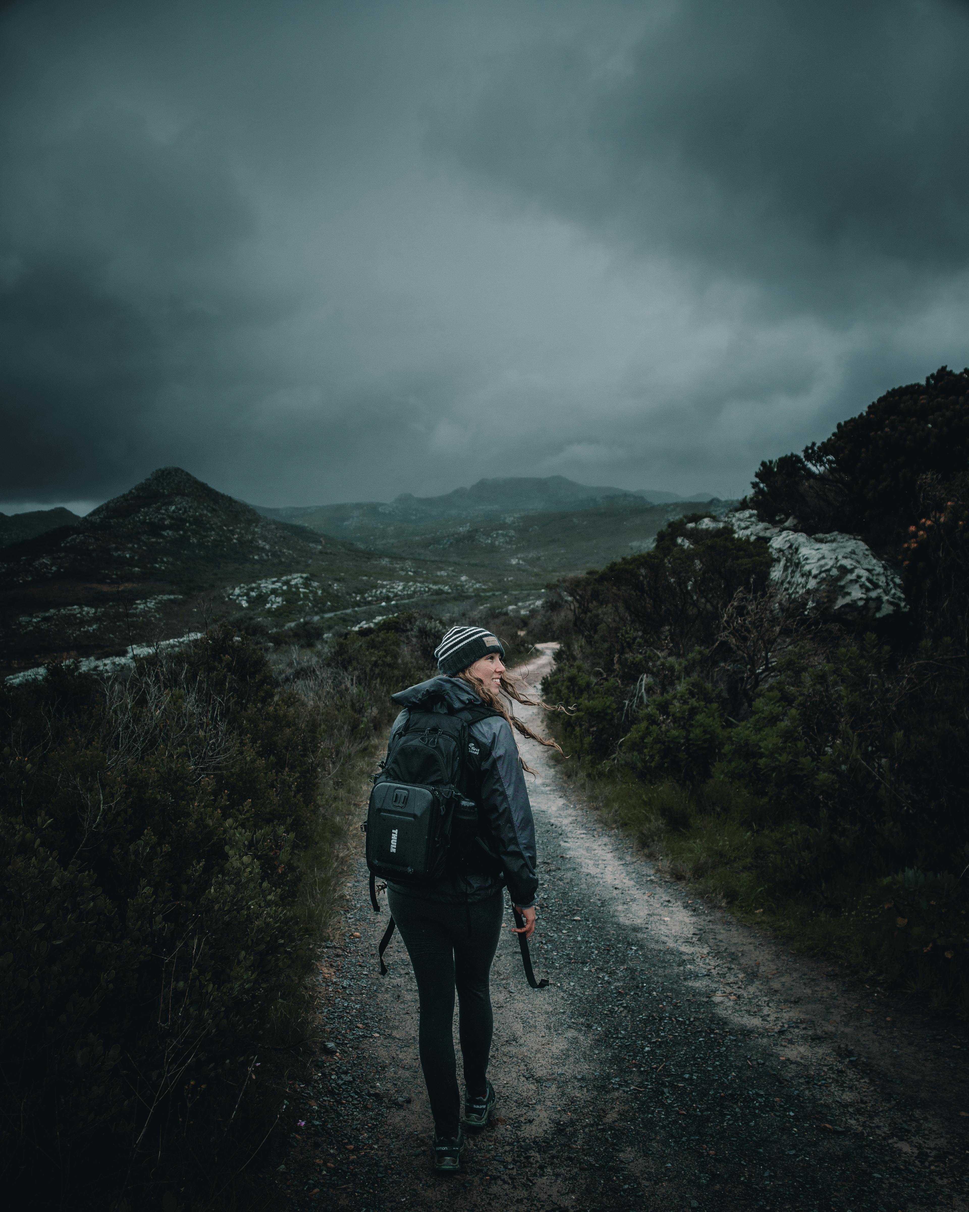 A woman hiker walks along a scenic mountain trail under cloudy skies in Cape Town, South Africa.
