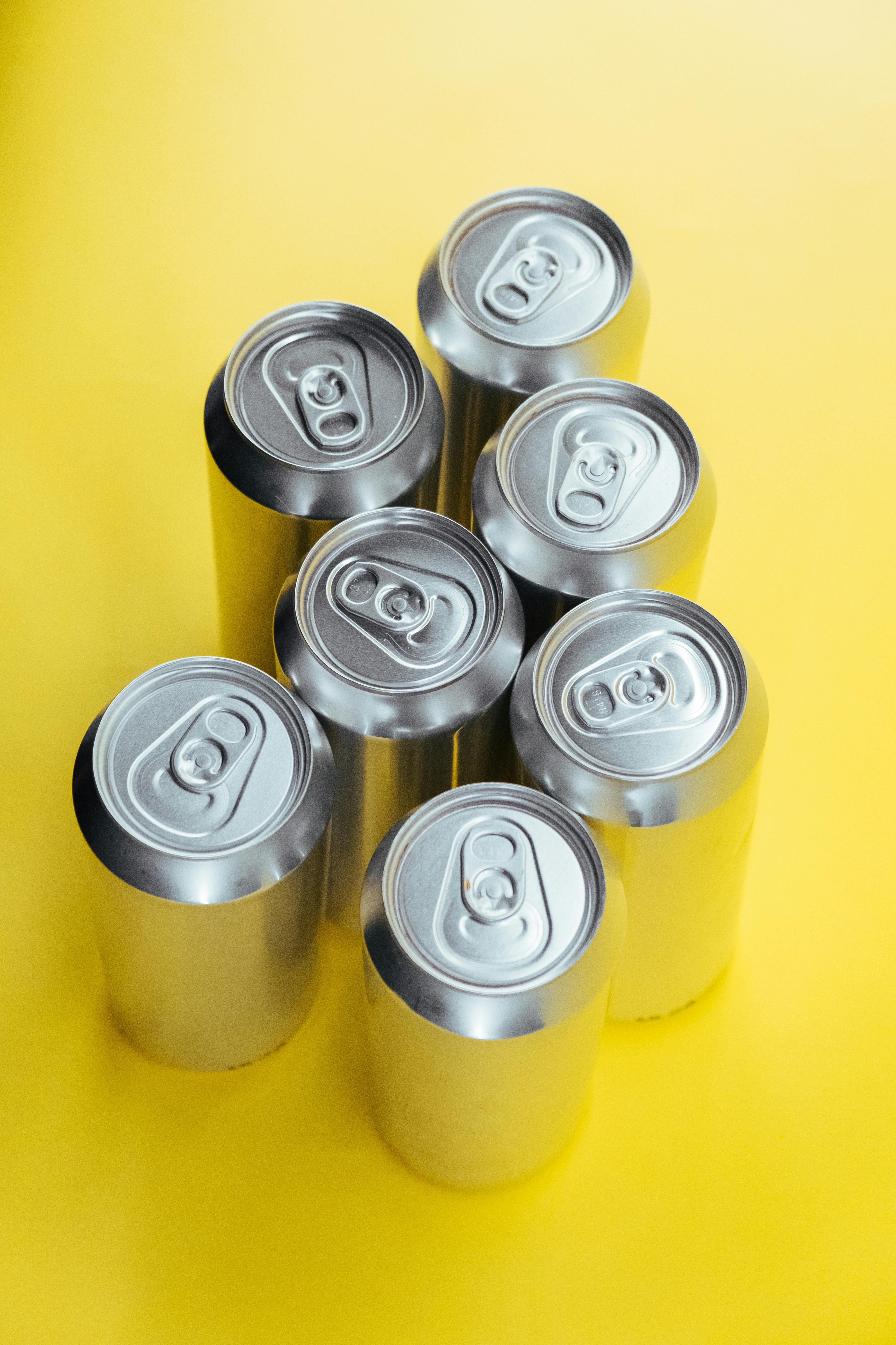 Top-down view of metal beverage cans artistically arranged on a bright yellow backdrop.