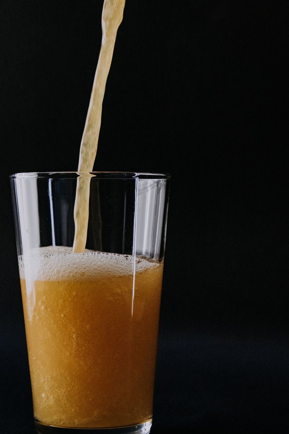 Golden beer being poured into a glass against a black background
