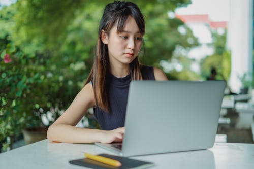 Concentrated young Asian female in casual outfit with long hair working on laptop in cafe