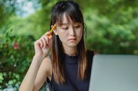 一位年轻的亚洲女学生正愉快地在咖啡馆的桌上用笔记本电脑做研究并记笔记
