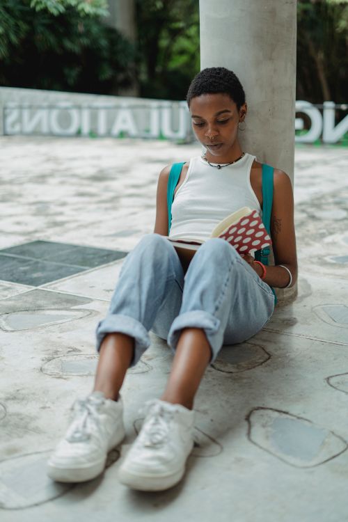 Free Focused young African American female student in casual clothes sitting on ground and reading notes in notebook Stock Photo