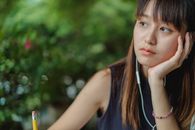 一位年轻女子一边听音乐，一边深思熟虑地思考着户外的学习笔记