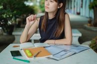 一位沉思的年轻亚洲女性坐在桌前，边做作业边在文案簿上做笔记