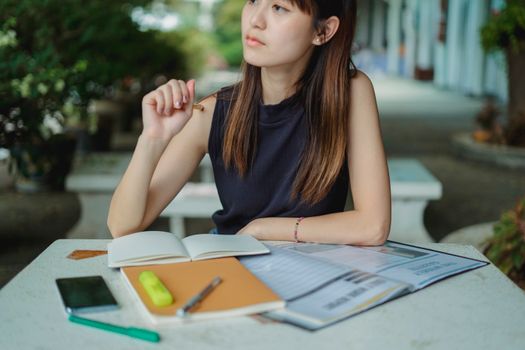 一位沉思的年轻亚洲女性坐在桌前，边做作业边在文案簿上做笔记