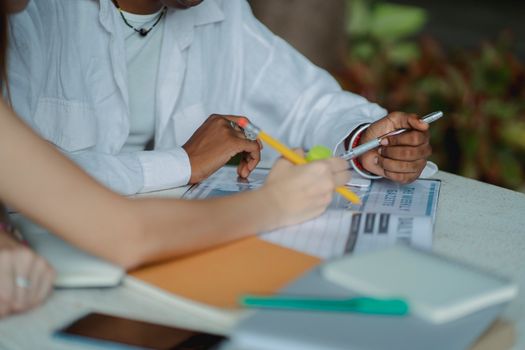Crop anonymous multiracial female students sitting at table and doing academic project together