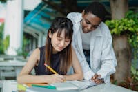 Two students working together outside, studying and discussing in a park setting.