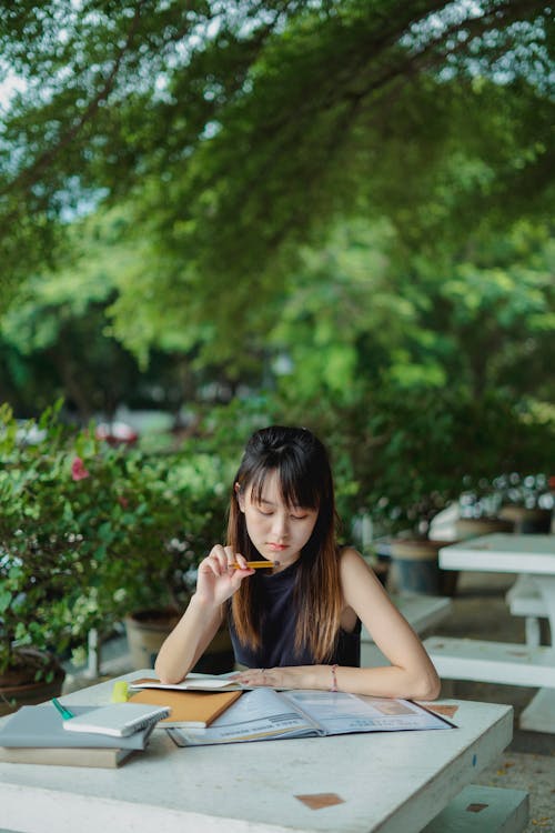 Free Young Asian lady studying with books outdoors in casual outfit in summer day at table Stock Photo