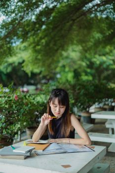 夏日户外餐桌上，一位年轻的亚洲女士穿着休闲服装在看书