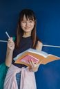 在蓝色背景下，一名年轻的亚洲女子拿着笔记本和笔微笑