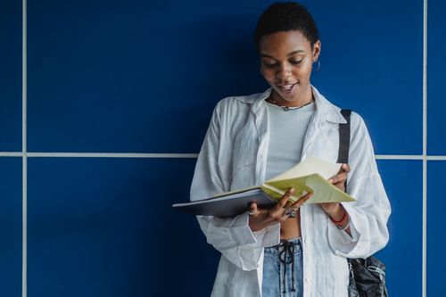Free Black female student in casual outfit standing with notebook and folder on blue background Stock Photo