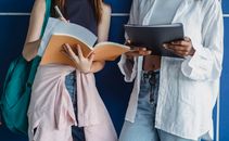 Crop faceless multiethnic women standing on blue background in casual clothes with notebook with pen and folder