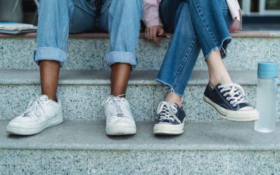 Crop anonymous multiracial women in casual clothes sitting on stairs with water bottle and papers in daytime