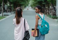 Back view of diverse female students carrying backpacks and supplies for university while talking in park