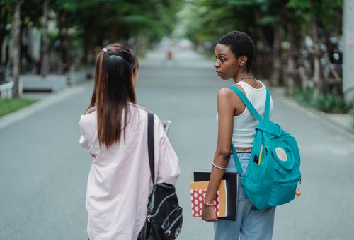 Free Back view of diverse female students carrying backpacks and supplies for university while talking in park Stock Photo