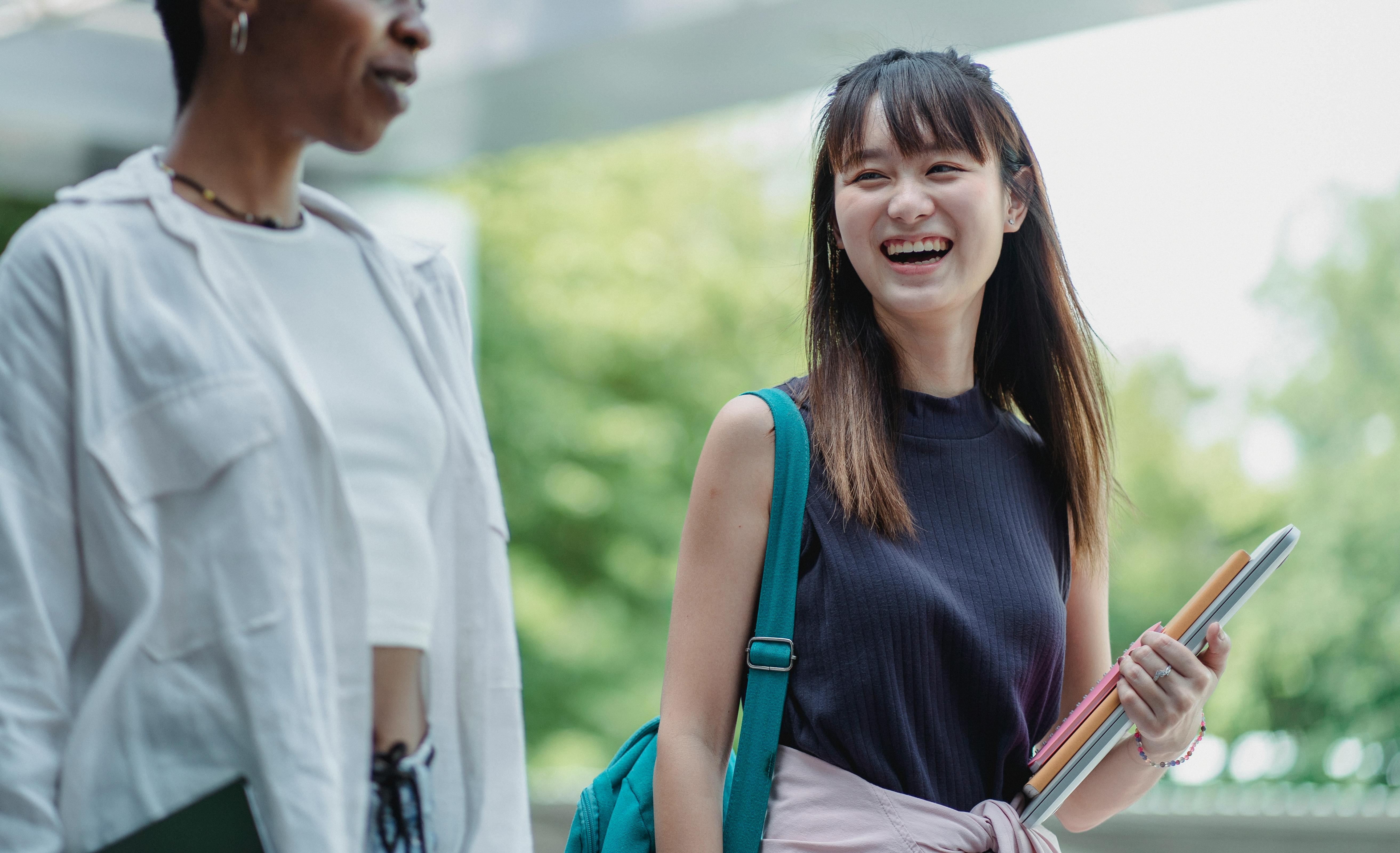 positive asian student laughing while walking with ethnic friend