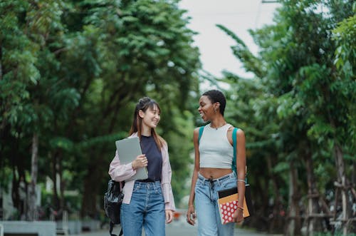 Smiling multiethnic girlfriends walking along green alley