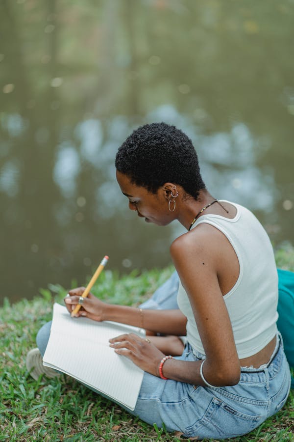 Serious black student writing essay in notebook in park