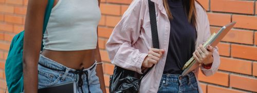 Free Crop anonymous black lady with backpack and female friend with netbook walking near university building during break Stock Photo