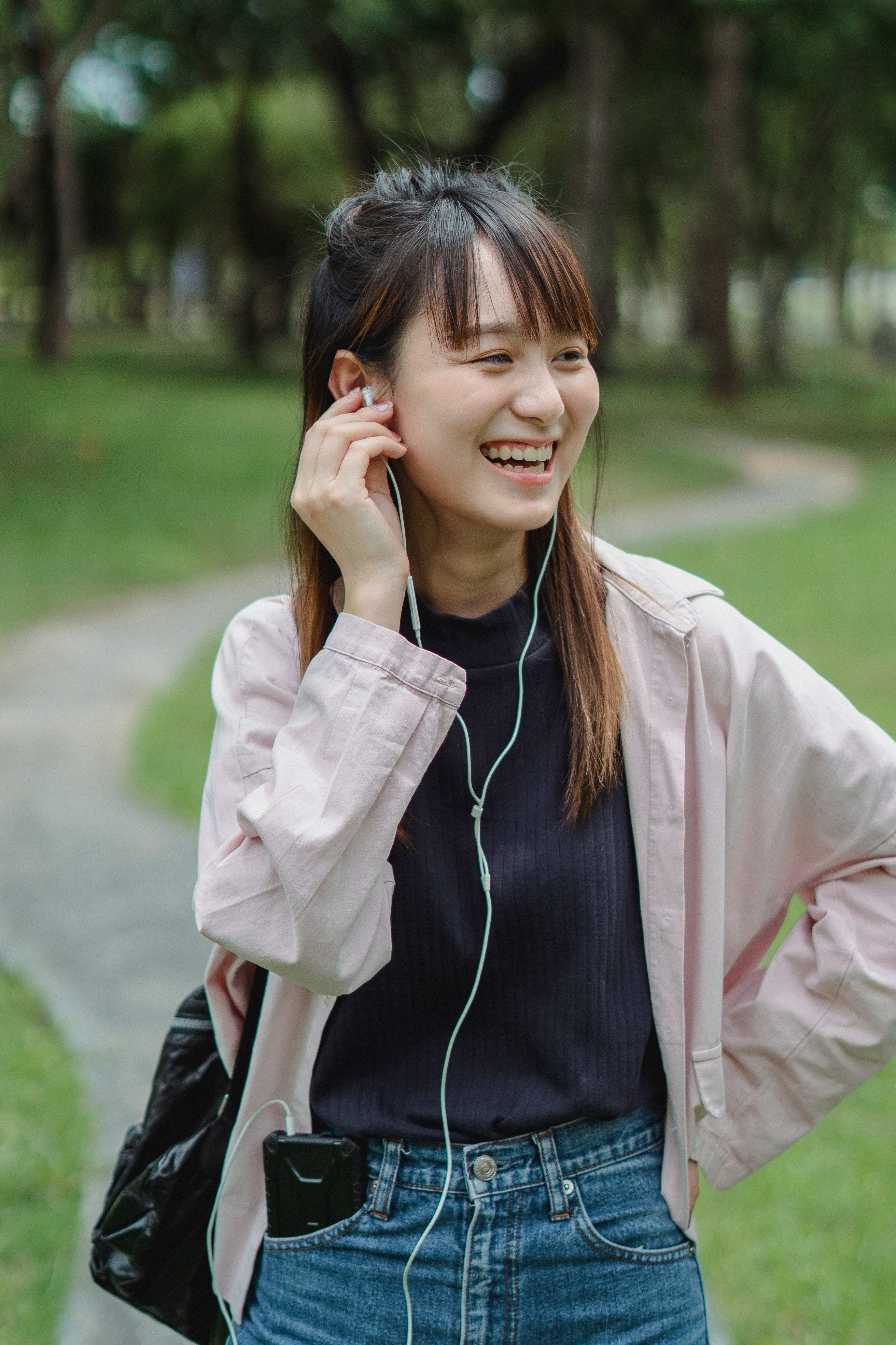 阳光明媚的日子里，一位戴着耳机的开朗年轻女子漫步在绿色的公园里，一边欣赏音乐