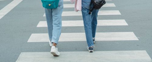 Free Back view of anonymous female pedestrians with backpacks wearing jeans and sneakers crossing asphalt road with zebra crossing in daytime Stock Photo