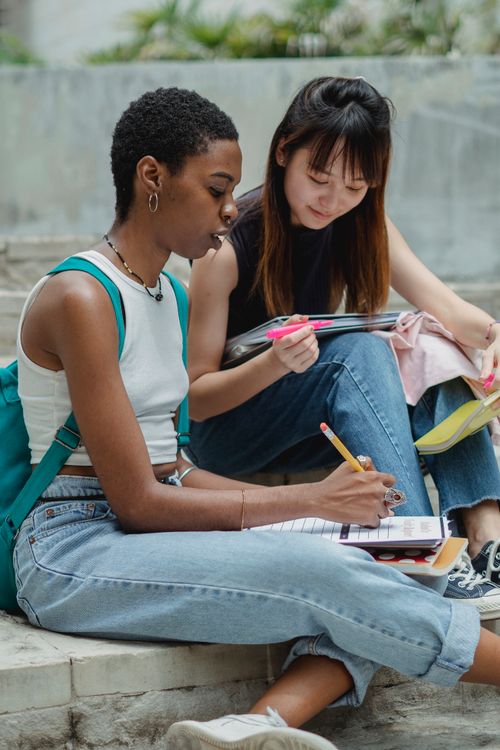 Free Concentrated black female student explaining project details to smiling Asian female friend while spending time together in urban street Stock Photo