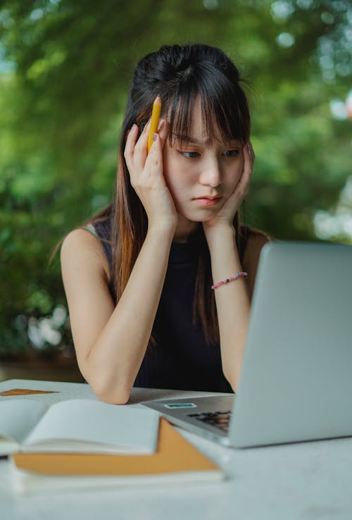 Mujer Asiática Joven Pensativa Que Trabaja En La Computadora Portátil En El Café De La Calle